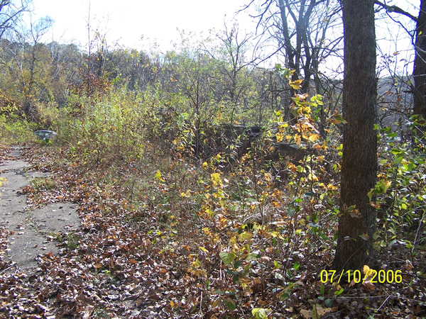 The remains of the decorative retaining wall at the Devil's Elbow, also showing the old concrete pavement. A car passing on modern U.S. 14 is visible on the left.