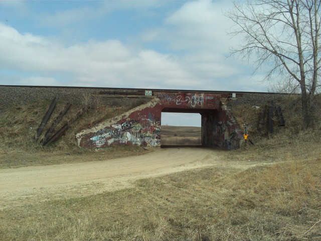 Another railroad underpass, east of Winnipeg Junction, with "Territorial Pissings". The road makes a rather sharp curve as it passes under the tracks.